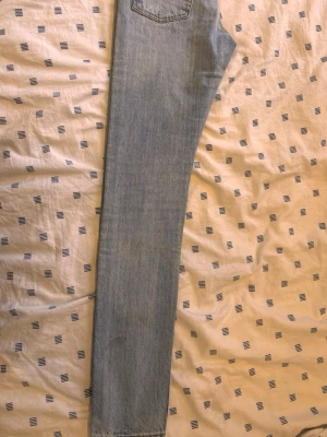 Levis Ljusblå slitna jeans med knappar - Ljusblå jeans med slitningar och knappar i gylfen. Jeansen har klassisk femficksdesign och orange detaljer vid fickorna. Materialet är denim och passformen är rak. Perfekt för dig som gillar en avslappnad och trendig look.