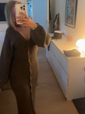 Brun lång stickad klänning med knappar - Säljer min stickade långklänning från gina då den inte kommer till användning för mig! Den är helst slutsåld på ginas hemsida. Aldrig använd men prislappen är tyvärr borttagen. I storlek xs! Pris går att diskuteras!💘