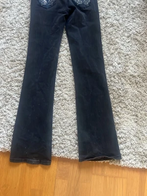 Svarta bootcut jeans med detaljer - Säljer ett par svarta bootcut jeans från Madlady i xtall 36, med snygga detaljer på bakfickorna. Jeansen har en klassisk femficksmodell och är tillverkade i ett stretchigt denimtyg som sitter skönt. Perfekta för dig som gillar en lite vidare passform nedtill. 