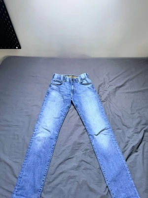 Blå raka jeans från Lee - Säljer ett par klassiska blå jeans från Lee med rak passform och fem fickor. Jeansen har en snygg tvättad look och är tillverkade i slitstarkt denimtyg. Perfekta för dig som gillar tidlös stil och vill ha ett par jeans som funkar till det mesta.