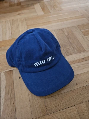 Blå keps från Miu Miu - Snygg blå keps från Miu Miu med vit broderad logga framtill. Klassisk böjd skärm och justerbar baksida. Perfekt accessoar för en trendig och avslappnad stil.