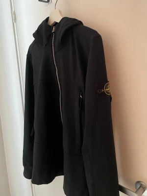 vindjacka - Stone Island - Snygg marinblå/mörkblå herr vindjacka från Stone Island med huva och dragkedja framtill. Lätt fleece inuti. Jackan har klassisk patch på ärmen och sportiga ränder på huvkanten. SISTA bilden är i direkt solljus. 