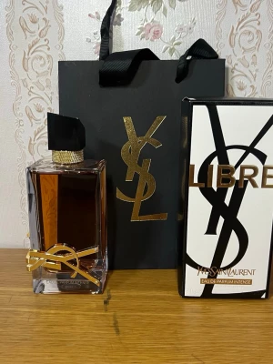Yves Saint Laurent Libre Eau de Parfum - Exklusiv parfym från Yves Saint Laurent, Libre Eau de Parfum Intense. Flaskan är rektangulär med transparent glas och bär en varm bärnstensfärgad vätska. Dekorerad med en elegant guldfärgad YSL-logga och svart, guldmönstrad kork. Perfekt för dig som vill ha en lyxig doft.