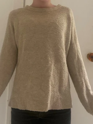 Beige stickad tröja från Monki - Mysig beige stickad tröja från Monki med rund halsringning och långa ärmar. Tröjan har en enkel, rak passform och ribbade muddar vid hals, ärmslut och nederkant. Perfekt för lager på lager och chill dagar.