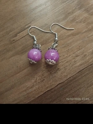 Lila pärlörhängen med silverdetaljer - Snygga örhängen med lila pärlor och silvriga metalldetaljer. Rund form och enkel krok för att hänga i örat. Perfekta för att ge din stil en färgklick.