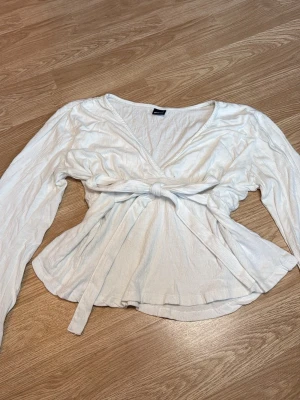 Topp från Gina Tricot - Vit långärmad topp som går att knyta både framme vid midjan men även bak vid ryggen. Från Gina Tricot i storlek L
