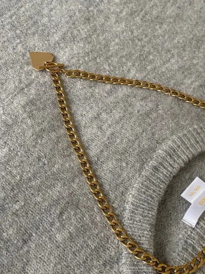 Guldigt halsband med hjärthänge - Snyggt halsband i guldfärgad rostfritt. Kedjan är chunky och har ett geometriskt hjärthänge samt ett dekorativt T-lås framtill. Perfekt accessoar för att lyfta din outfit med en trendig touch.