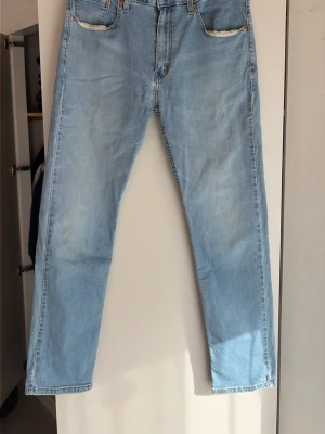 Ljusblå raka jeans från Levi's - Säljer ett par klassiska ljusblå jeans från Levi's med rak passform och fem fickor. Jeansen har en vintagekänsla, ikonisk patch bak och röda Levi's-taggen på bakfickan. Tillverkade i slitstark denim, perfekta för en avslappnad och tidlös stil.