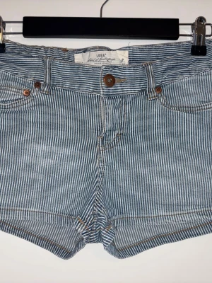 Randiga jeansshorts från L.O.G.G. - Säljer ett par blåvit randiga jeansshorts från L.O.G.G. by H&M. Klassisk femficksmodell med knapp och dragkedja framtill. Snygga kontrastsömmar och midwaist passform. Perfekta till sommaren!