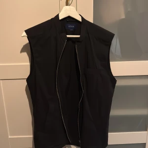 Svart väst från Eton med dragkedja - Stilren svart väst från Eton med rak passform och diskret bröstficka. Västen har en snygg dragkedja framtill och är perfekt för att ge din outfit en clean och modern touch.