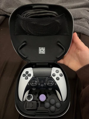 PlayStation DualSense Edge handkontroll - PlayStation DualSense Edge handkontroll i svart och vitt med utbytbara spakar och knappar. Kommer i ett hårt fodral med extra tillbehör och USB-kabel. Ergonomisk design med texturerat grepp och avancerade funktioner för PS5.