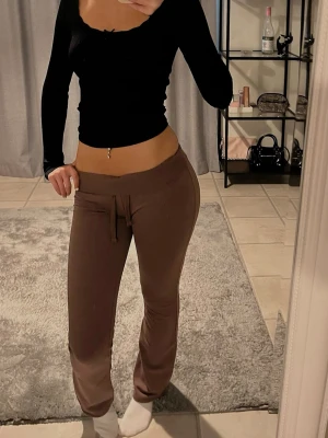 Nelly mjukisbyxor - Säljer ett par bruna mjukisbyxor med dragsko i midjan och raka ben. Byxorna har en enkel och clean look, perfekta för chill dagar. Materialet ser mjukt och bekvämt ut, och färgen är en snygg brun ton.