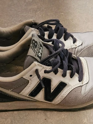 New Balance 996 vita/grå sneakers - Snygga New Balance 996 sneakers i vitt och grått med mörkblå detaljer och klassisk N-logga på sidan. Skorna har låga skaft, mörkblå snören och ovandel i mocka och mesh för en sportig look.