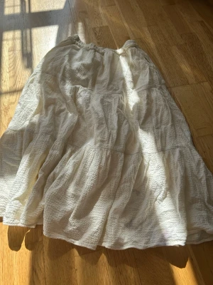 Vit volangkjol från Zara - Luftig vit kjol från Zara med volanger och resår i midjan. Kjolen har en strukturerad, krinklad bomullskänsla och faller snyggt i flera lager. Perfekt för en avslappnad och trendig look.