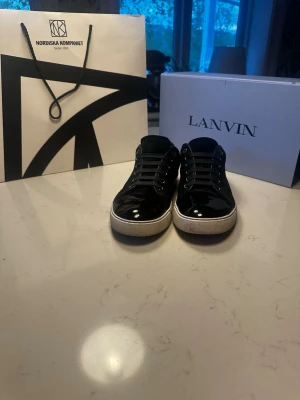 Lanvins INTRESSEKOLL! - Snygga svarta sneakers från Lanvin med blank finish och vita sulor. Skorna har låga skaft, svarta skosnören och metallhål för snörningen. Tillverkade i skinn med en stilren och klassisk design som passar till det mesta. Det är storlek 41 men skulle säga att dom passar bättre till 42. Tar gärna emot byten men har dom mest uppe för en koll på vad folk är värda att ge för dom, tveka inte på att skriva vid funderingar eller frågor🤗(kvitto finns från NK)