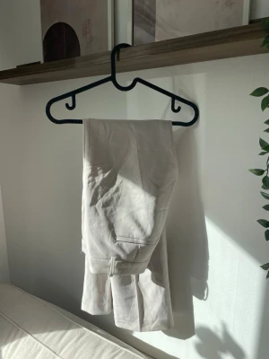 Beige kostymbyxa lågmidjade flare från BIKBOK - Stilrena beige kostymbyxor med pressveck och utvidgade ben. Byxorna har hällor för skärp, sidofickor och är lågmidjad. Perfekta för en clean och uppklädd look.