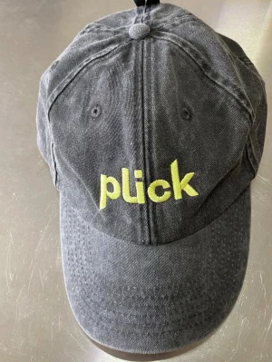 Svart plick keps - Snygg svart keps i tvättad bomull med justerbart spänne bak och broderad gul Plick-logga framtill. Klassisk dad cap-modell med böjd skärm och ventilerande hål. Perfekt accessoar för en avslappnad streetstyle-look.