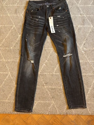 Svarta distressed jeans från Purple brand  - Snygga svarta jeans från Purple brand med slitna detaljer och hål vid knäna. Modellen är slim fit med klassisk femficksdesign och orangea sömmar. Jeansen har en cool tvättad look och är tillverkade i denim. Dem är i storlek 30, om ni har några frågor är det bara att fråga 😀