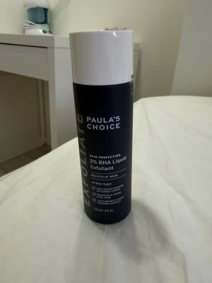 Paula's Choice 2% BHA Exfoliant - Populär exfolierande toner från Paula's Choice med 2% BHA (salicylsyra). Svart cylinderformad flaska med vit kork. Passar alla hudtyper och hjälper till att rengöra porer och jämna ut hudtonen. Perfekt för dig som vill boosta din hudvårdsrutin.