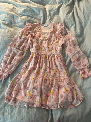 Blommig sommarklänning - Säljer denna jätte söta blommiga rosa klänningen perfekt till sommaren. Den är rosa med gula, rosa och gröna detaljer med lite volang och spets detaljer. Storlek 36 men passar 34 också, använd endast en gång. 
