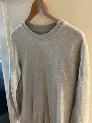 Grå basic sweatshirt - Enkel och stilren grå sweatshirt med rund halsringning och långa ärmar. Tröjan är tillverkad i mjukt material och har ribbade muddar vid hals, ärmslut och nederkant. Perfekt för en avslappnad look.