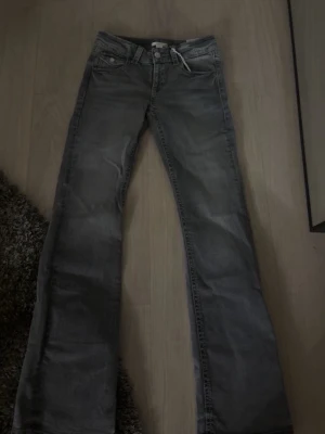 Grå bootcut jeans med låg midja - Snygga grå jeans med bootcut passform och låg midja. Jeansen har klassiska fem fickor och dragkedja med knapp. Perfekta för en avslappnad och trendig look.