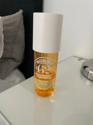 Brazilian Crush Cheirosa 62 Parfymmist - En parfymmist från Sol de Janeiro med doft av pistage och salt karamell. Flaskan är genomskinlig med guldfärgad vätska och har en stor vit kork. Perfekt för dig som gillar söta och varma dofter.