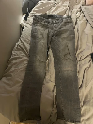 Grå raka jeans från Jack & Jones - Säljer ett par grå jeans från Jack & Jones i rak modell. Jeansen har klassisk femficksdesign, knappgylf och är tillverkade i bomullsdenim. Perfekta för en avslappnad och stilren look.