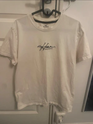 Vit t-shirt från Hollister - Vit t-shirt från Hollister med svart broderad text på bröstet. Mycket bra skick