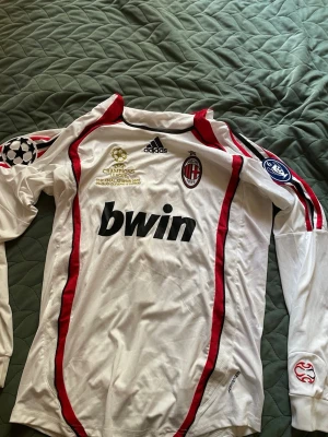 AC Milan långärmad Ronaldinho tröja - Säljer en vit långärmad AC Milan matchtröja från Adidas med Ronaldinho och nummer 80 på ryggen. Tröjan har röda och svarta detaljer, Champions League-märken på ärmarna och Bwin som sponsor på bröstet. Perfekt för dig som älskar fotboll och klassiska retrotröjor.Och storlek L