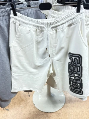 Vita shorts med snörning från Fendi - Säljer ett par vita shorts från Fendi med snörning i midjan och två sidofickor. Shortsen har en stor svart logga längs ena benet och är perfekta för en avslappnad stil. Tillverkade i mjukt material för extra komfort.