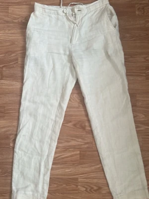Beiga linnebyxor - Snygga beiga linnebyxor med avslappnad passform och raka ben. Byxorna har sidfickor fram, två bakfickor med knapp och elastisk midja bak. Perfekta för en chill och stilren look under varma dagar.