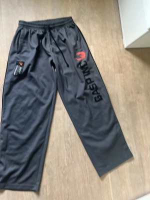 Svarta träningsshorts från GASP - Säljer ett par svarta träningsshorts från GASP med elastisk midja och stort tryck på sidan. Materialet är polyester och designen är sportig med en cool logga i orange. Perfekta för gymmet eller andra sportaktiviteter.