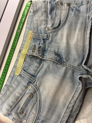 Ljusblå denimshorts med nitar - Måttet rakt över är 40cm.