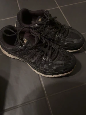 Svarta Nike sneakers p6000 - Svarta Nike sneakers med cool design, mesh- och skinnpaneler samt vita sulor. Skorna har klassisk snörning och diskret Nike-logga på tungan. Perfekta för dig som gillar sportig och street-inspirerad stil.