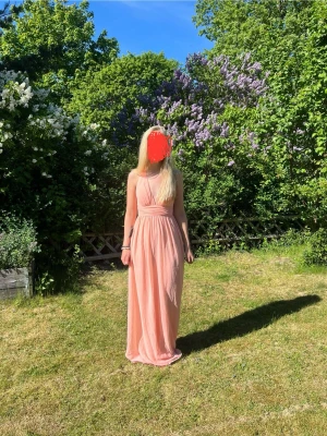 Ljusrosa långklänning med öppen rygg - Säljer en ljusrosa långklänning med omlottdetalj och öppen rygg. Klänningen har smala axelband som korsas i ryggen och ett fint fall i tyget. Perfekt för sommarens alla tillfällen eller som balklänning! Har inlägg i brösten så man ej behöver ha något under💕