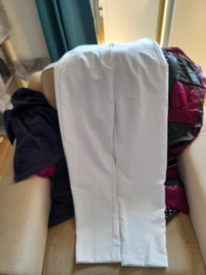Vita raka kostymbyxor - Säljer ett par stilrena vita kostymbyxor med rak passform och pressveck. Byxorna har en klassisk look och passar perfekt till en dressad outfit. Materialet ser ut att vara en mjuk och slät textil som ger en snygg siluett.
