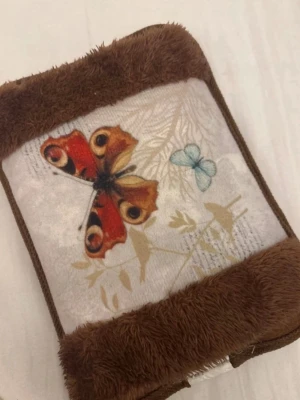 Electric hot water bottle  - Mysig brun värmedyna med mjuk pälsimitation och dekorativt fjärilsmotiv på ena sidan. Rektangulär form och enkel att använda, perfekt för kalla dagar eller när du vill ha extra värme.