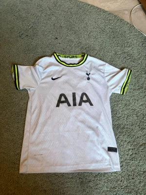 Tottenham Hotspur matchtröja Son 7 - Vit Tottenham Hotspur matchtröja från Nike med svarta detaljer, klubbmärke och sponsorlogga på bröstet. Neongula och svarta ränder vid krage och ärmslut. På ryggen står det 'SON' och nummer 7. Perfekt för fotbollsfans!