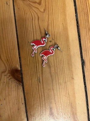 Röda flamingo örhängen - Örhängen i plast formade som röda flamingos. Glittrig sten vid fästet. Förmodligen nickel/oäkta.