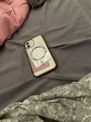 iPhone 11 med genomskinligt skal - Säljer en vit iPhone 11 från Apple med rundade hörn och stor skärm. Telefonen har ett genomskinligt skal med kortfack och ringhållare på baksidan. Perfekt för dig som vill ha både stil och funktion i vardagen.