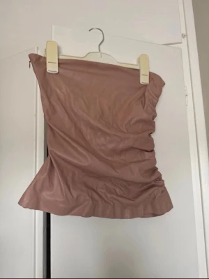 Rosa tubtopp  - Säljer en rosa tubtopp i ett glansigt syntetmaterial. Toppen är axelbandslös och har en lätt rynkad effekt på sidorna för en cool look. Perfekt att styla med jeans eller kjol för en trendig outfit.