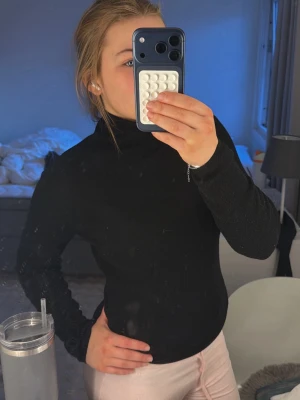 Svart polotröja  - Säljer en svart stickad polotröja med lång ärm och figurnära passform. Tröjan har en klassisk hög krage och är perfekt att styla till olika outfits. Materialet är mjukt och stretchigt för extra komfort.