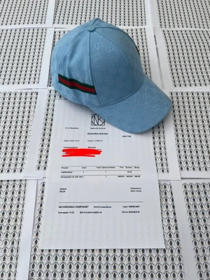 Ljusblå Gcii keps med G-mönster - Säljer en ljusblå keps från Gci med det klassiska G-monogrammet över hela tyget. Kepsen har en böjd skärm och en grön-röd rand på sidan som ger den en ikonisk look. Tillverkad i ett slitstarkt tyg som känns lyxigt och trendigt.