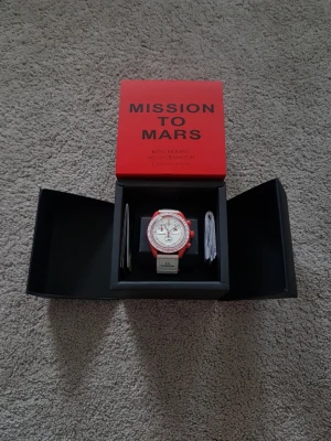 Omega x Swatch Mission to Mars klocka - Säljer en Omega x Swatch Mission to Mars från Bioceramic MoonSwatch Collection. Klockan har en vit urtavla med röda detaljer och röd boett, samt vit rem med Omega-logga. Snygg och unik design som sticker ut på handleden.