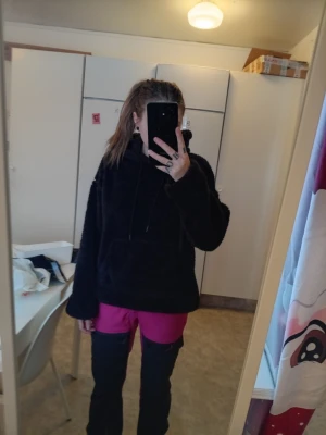 Svart fluffig hoodie med huva - Mysig svart hoodie med fluffigt material och stor huva. Tröjan har en rymlig magficka och dragsnören vid huvan. Perfekt för dig som gillar en avslappnad och cool stil.