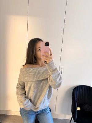 Beige off shoulder stickad tröja - Trendig beige stickad tröja med bred off shoulder-krage och avslappnad passform. Perfekt att styla med jeans för en chill look. Mjuk och skön, med långa ärmar och ribbade muddar. Materialet känns som en mysig ull- eller bomullsblandning.