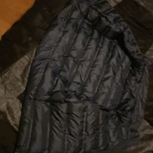 Blå pufferjacka - Säljer en snygg blå pufferjacka i bra skick. Perfekt för sommaren som kommer med sitt quiltade mönster. Jackan har en dragkedja framtill och är gjord av syntetmaterial.  Storlek 146/152 den har en liten spricka 