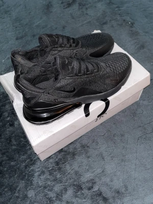Nike Air Max 270 helsvarta sneakers - Snygga helsvarta Nike Air Max 270 sneakers med stickad ovandel och stor synlig Air-enhet i hälen. Skorna har en sportig siluett, diskret Swoosh-logga och bekväm passform. Perfekta för dig som gillar stilrena och moderna sneakers.