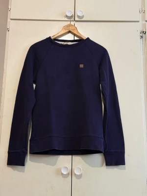 Mörkblå sweatshirt från Carhartt - En stilren mörkblå sweatshirt från Carhartt med rund halsringning och diskret logopatch på bröstet. Tröjan har långa ärmar, ribbade muddar och är tillverkad i mjukt bomullsmaterial. Perfekt för en avslappnad och trendig look.